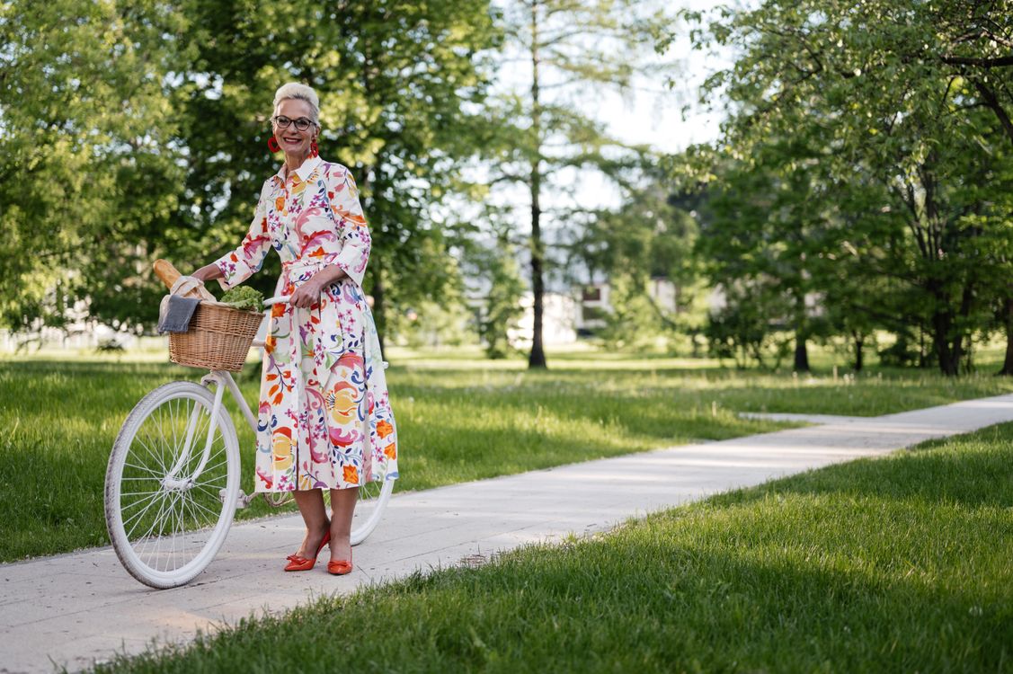 Older woman standing with her bicycle on a park path, illustrating personal priorities when considering life insurance for parents.