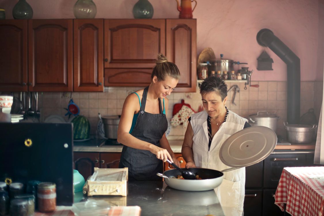 Two adult women cooking together in a kitchen, illustrating the family relationships behind life insurance for parents.