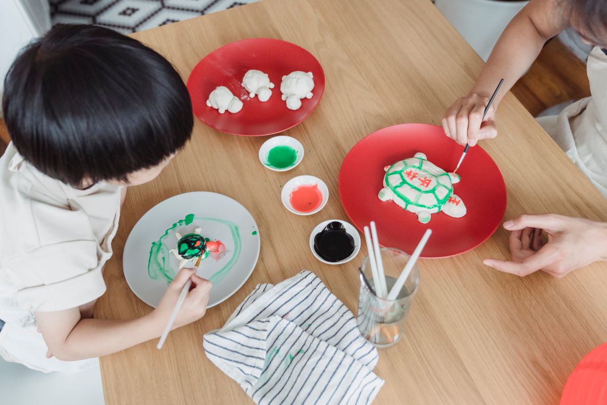 Overhead view of a child and adult painting small clay figures together, illustrating family priorities when considering life insurance for children.