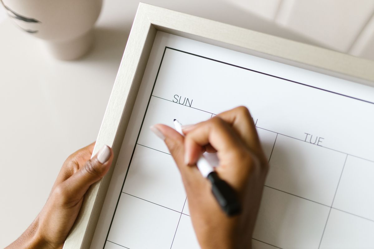 Hands write on a calendar to organize Medicare and group health insurance enrollment and coverage transition dates.