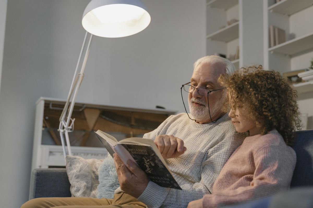 Grandfather and granddaughter reading a book together, illustrating the family conversation behind a gift of life insurance for children.